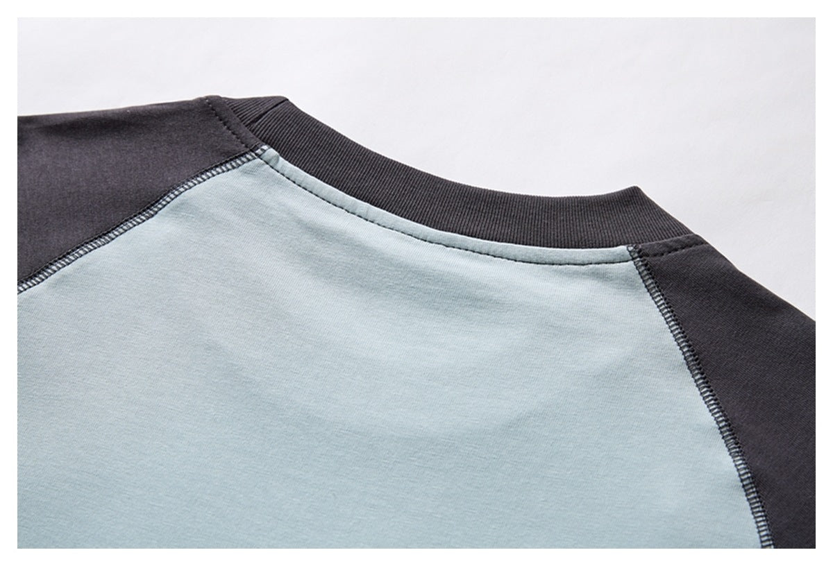 Close-up of a pale blue and charcoal raglan top's ribbed neckline and shoulder seams.