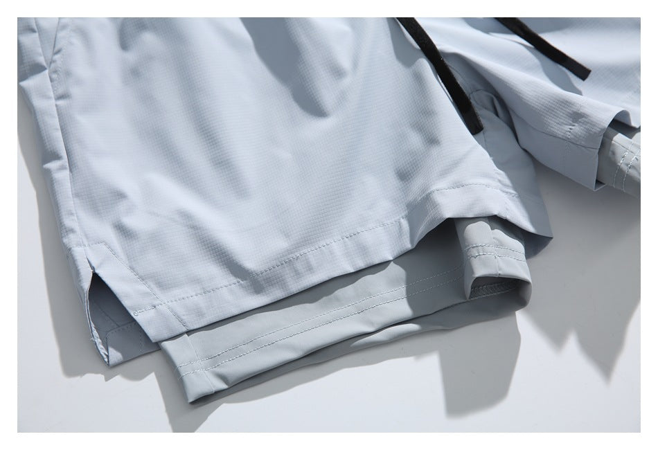 Close-up of the hem and side slit on pale blue-gray shorts, with a black drawstring partly visible.
