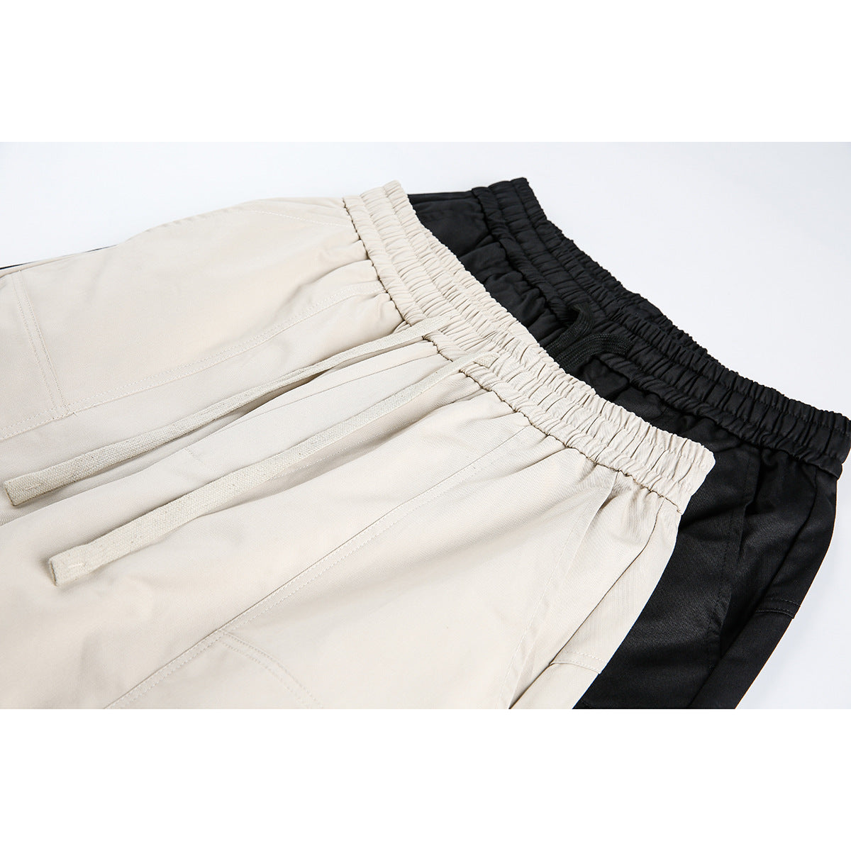 Close-up of beige and black pants showing gathered elastic waistbands, drawstrings, and stitched panels.
