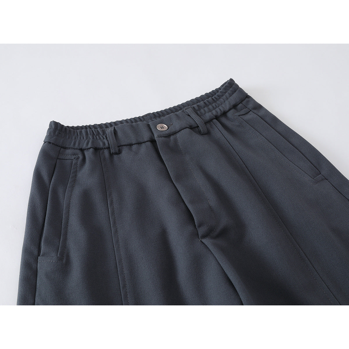 Close-up of charcoal wide-leg trousers showing the elasticated waistband, button closure, pleats and front pockets.