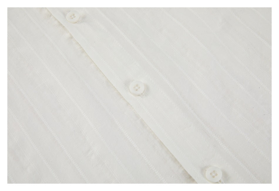 Close-up of a white shirt’s button placket with three white buttons and subtle vertical stripes.
