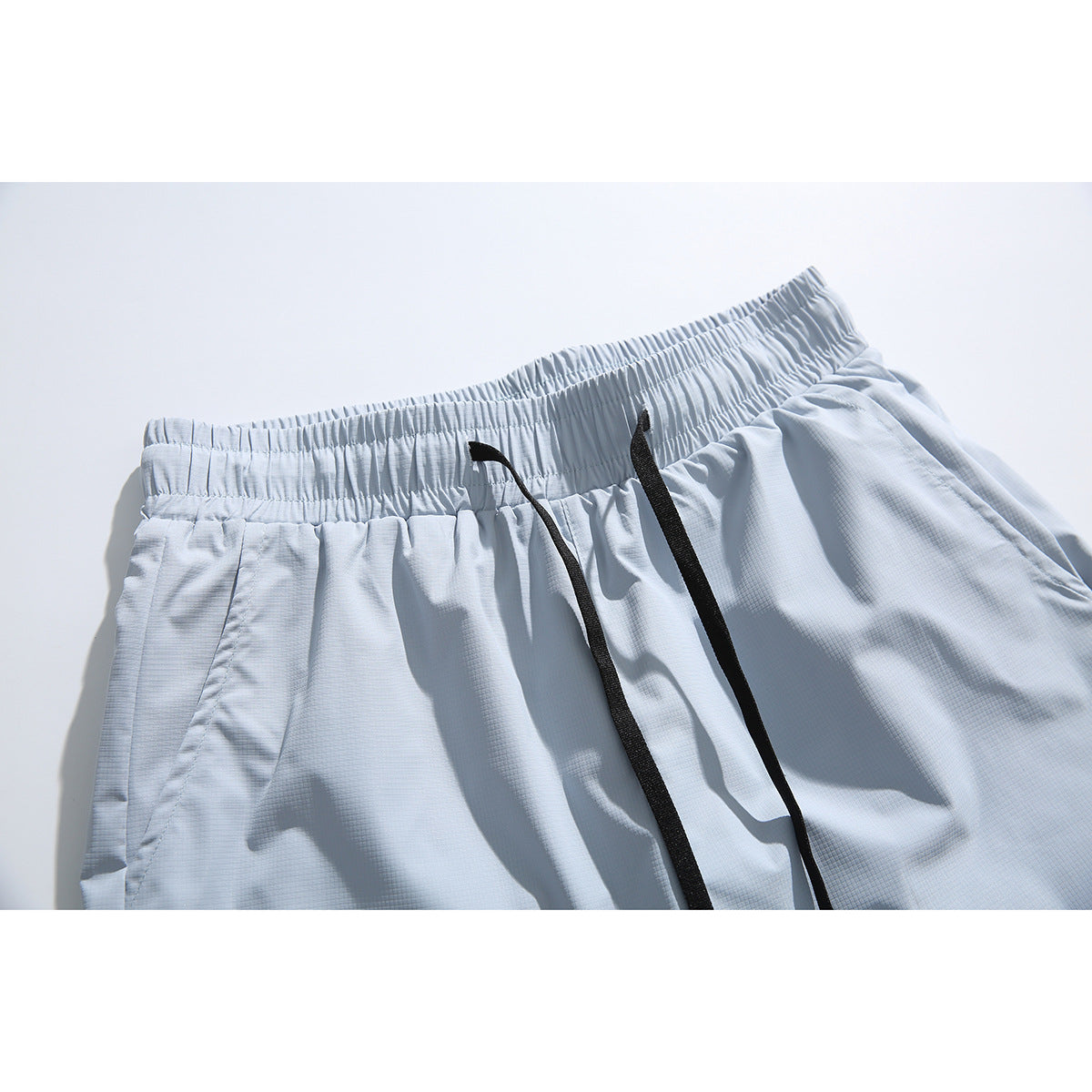 Close-up of pale blue-gray shorts showing an elastic waistband and long black drawstrings.