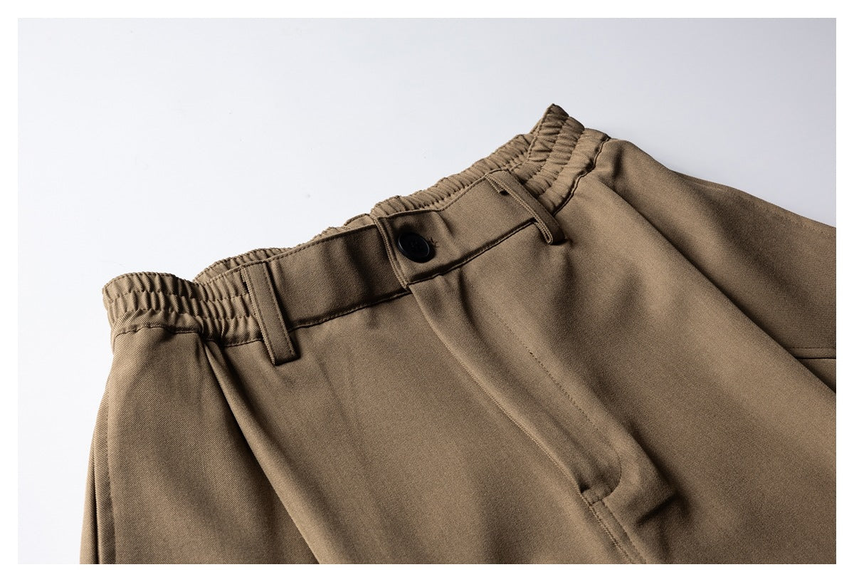 Close-up of brown shorts showing the elasticated waistband, belt loops, black button and front fly.
