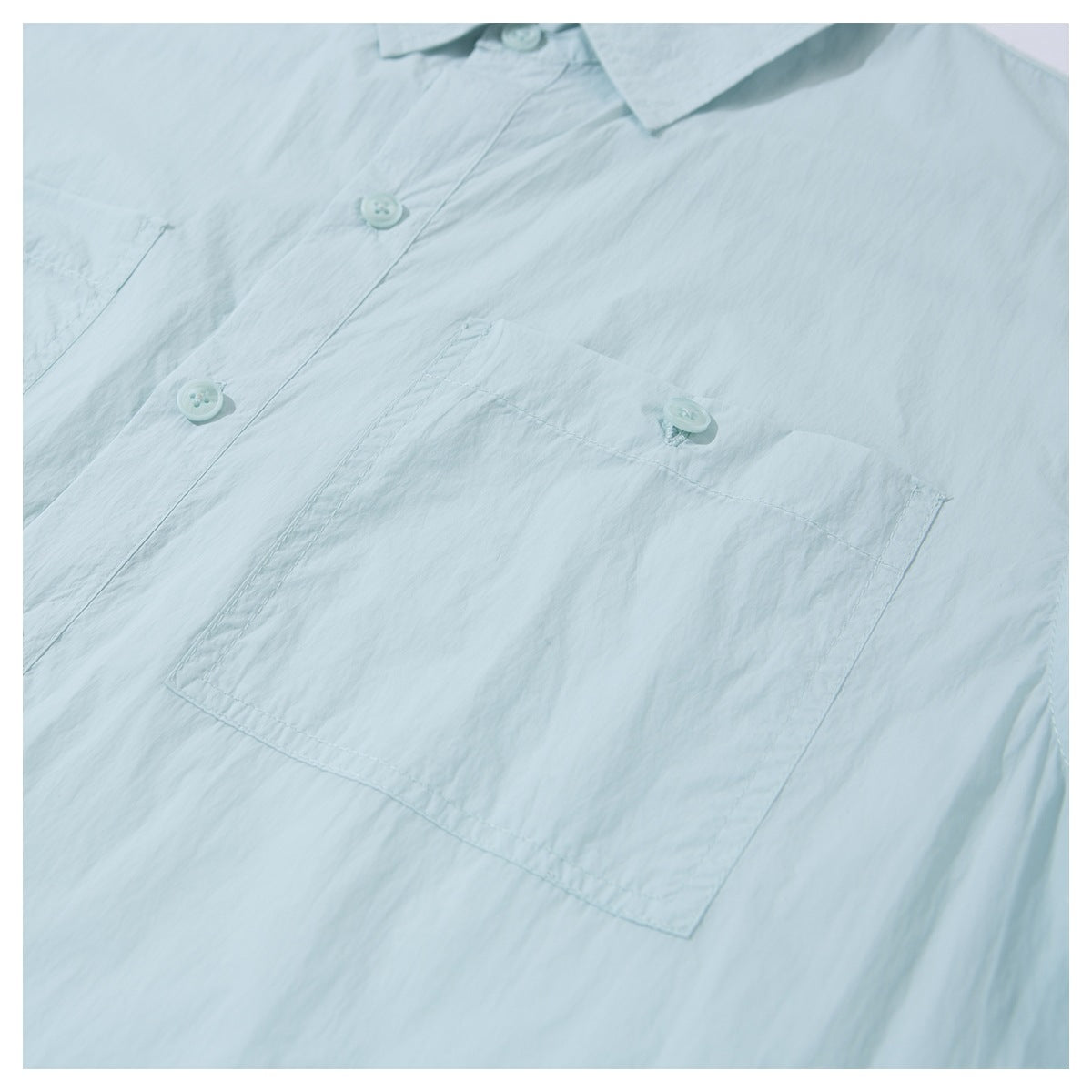 Close-up of a pale mint button-up shirt showing its collar, buttons, and large chest pocket.