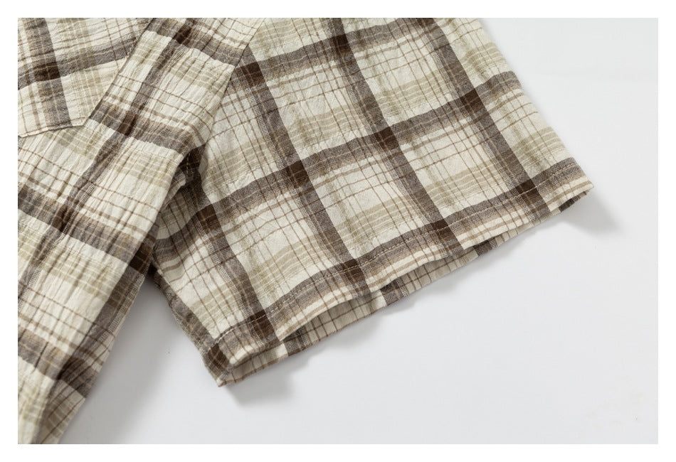 Close-up of the stitched edge of beige and brown plaid fabric against a white background.