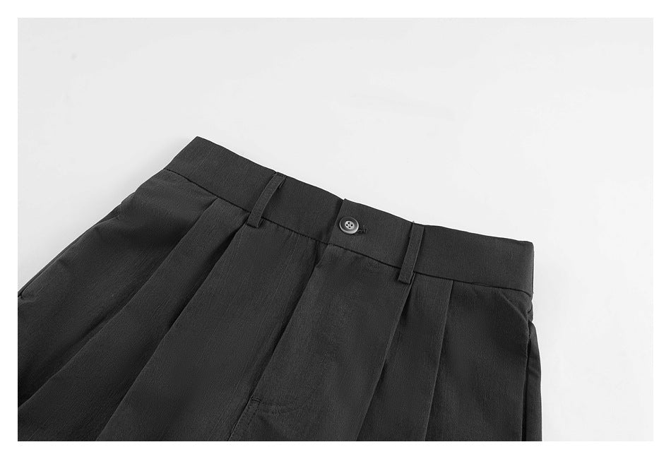 Close-up of black shorts showing the buttoned waistband, belt loops, front pleats and side pockets.