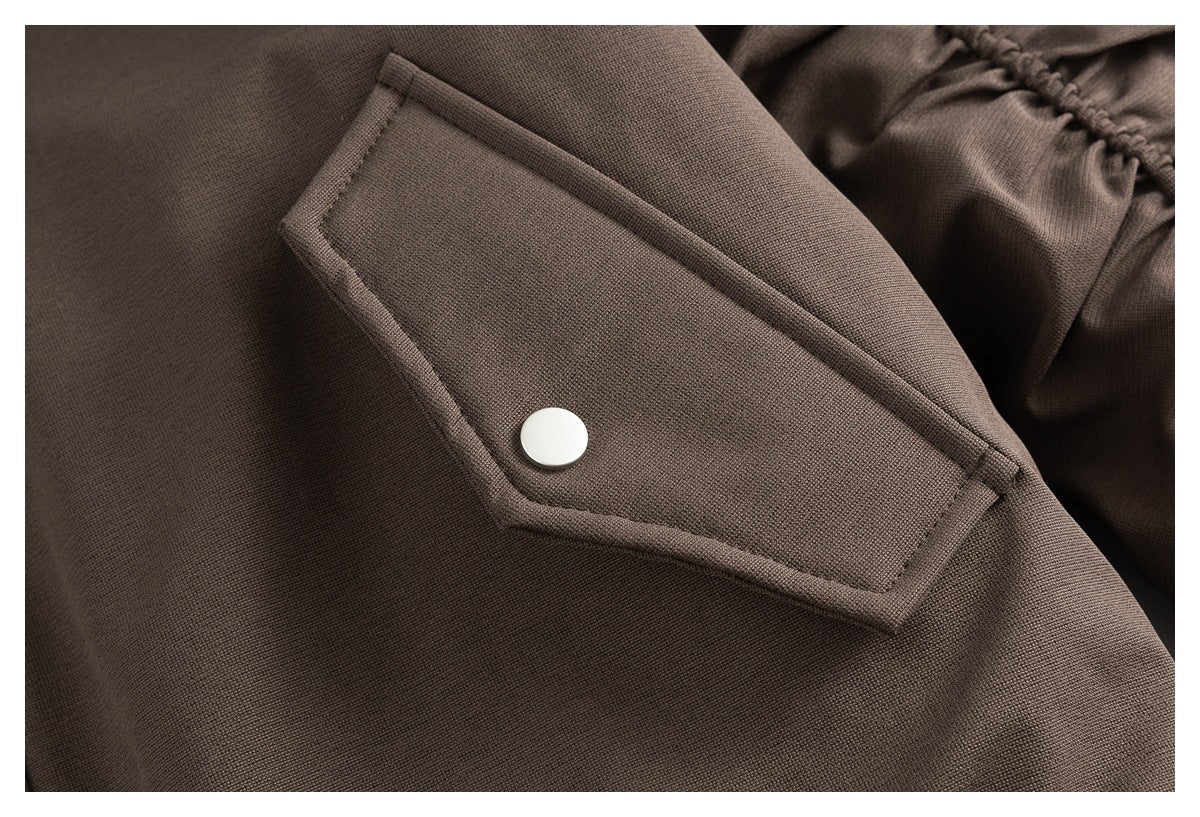 Close-up of a brown jacket pocket flap with a white snap button and gathered sleeve fabric nearby.