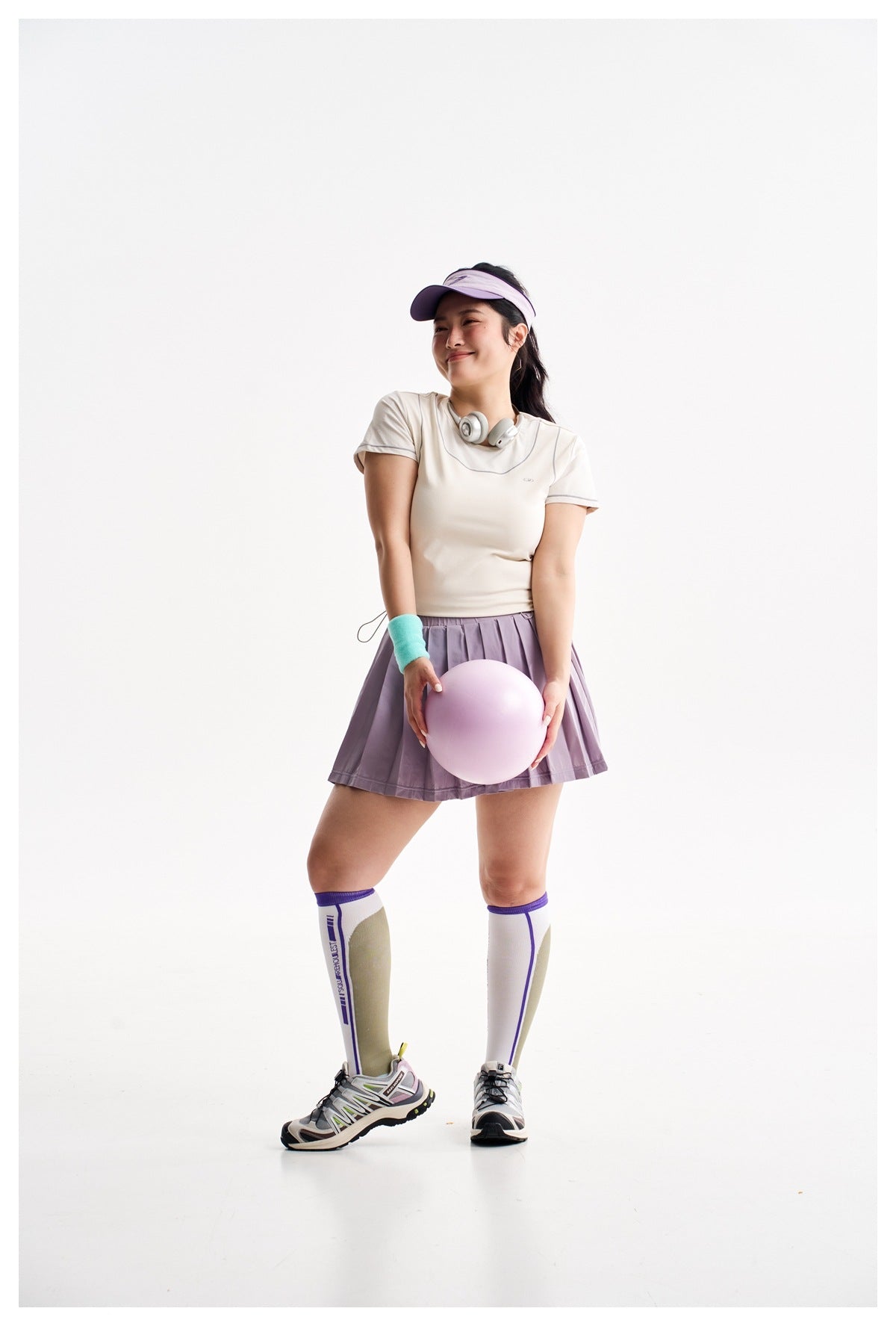 Model wearing a lavender pleated skirt with an ivory top, visor, knee-high socks, and sneakers.