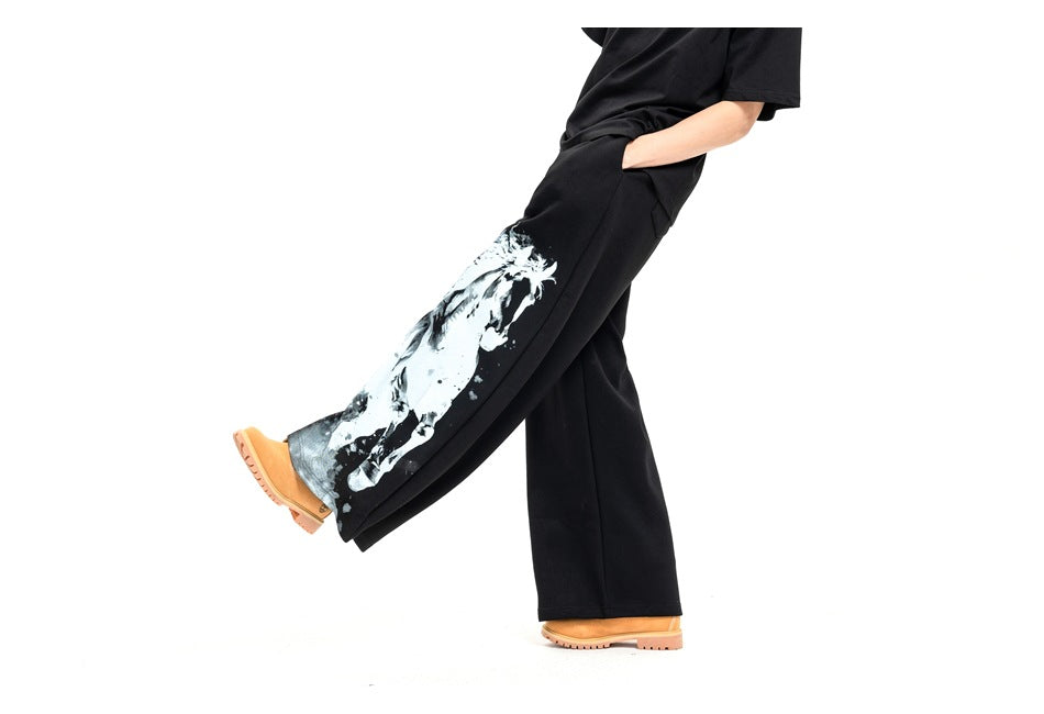Angled view of a model wearing black wide-leg pants with a large white horse graphic on one leg.