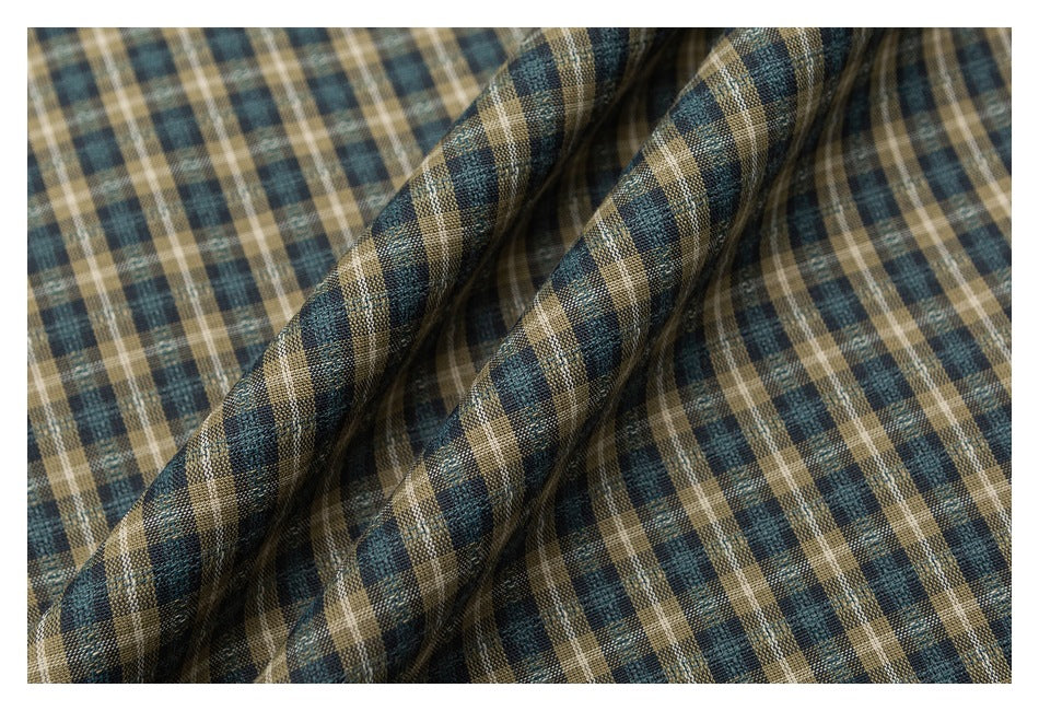Close-up of draped plaid fabric in muted teal, tan, cream, and dark brown.