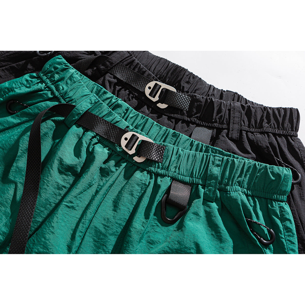 Close-up of teal and black shorts showing elastic waistbands, webbing straps, metal buckles and clips.