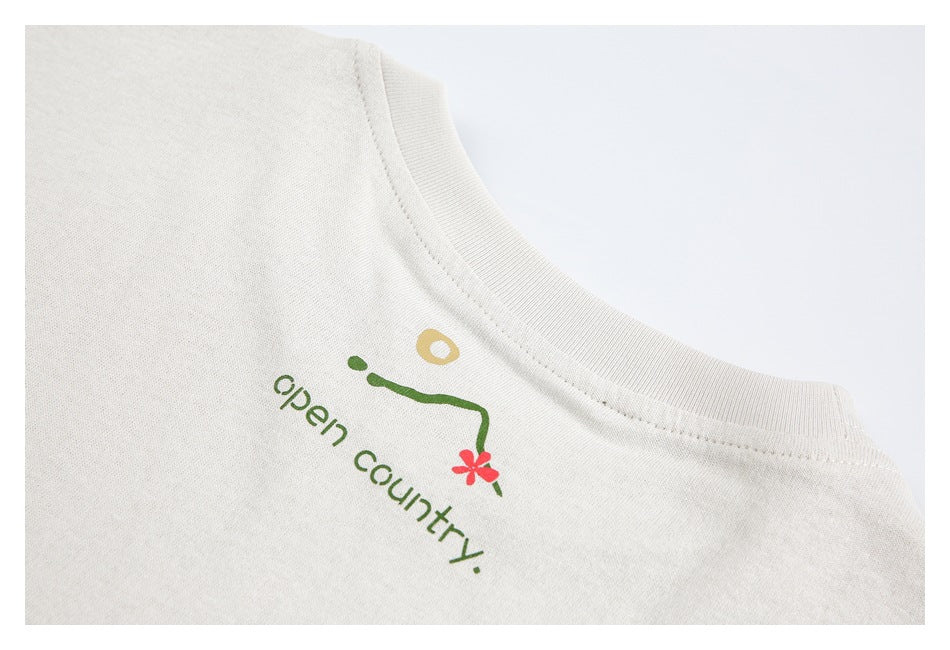 Close-up of an off-white crew neck with a small green, red, and gold graphic and “open country” text.