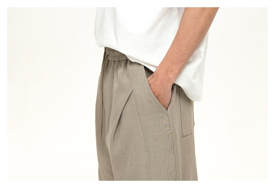 Close-up side view of a model wearing taupe drawstring-waist trousers with a large slanted pocket.