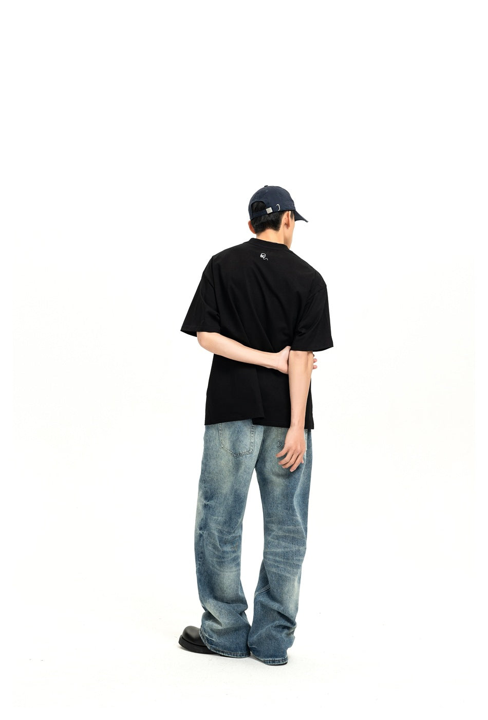 Back view of a model wearing a plain black short-sleeve T-shirt with a small white mark below the collar.