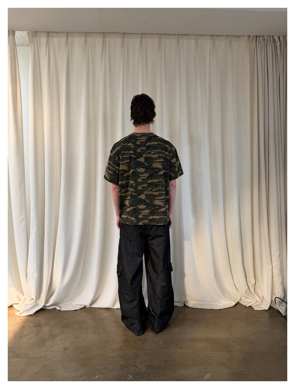 Back view of a model wearing a green and brown camouflage T-shirt and loose black cargo jeans.