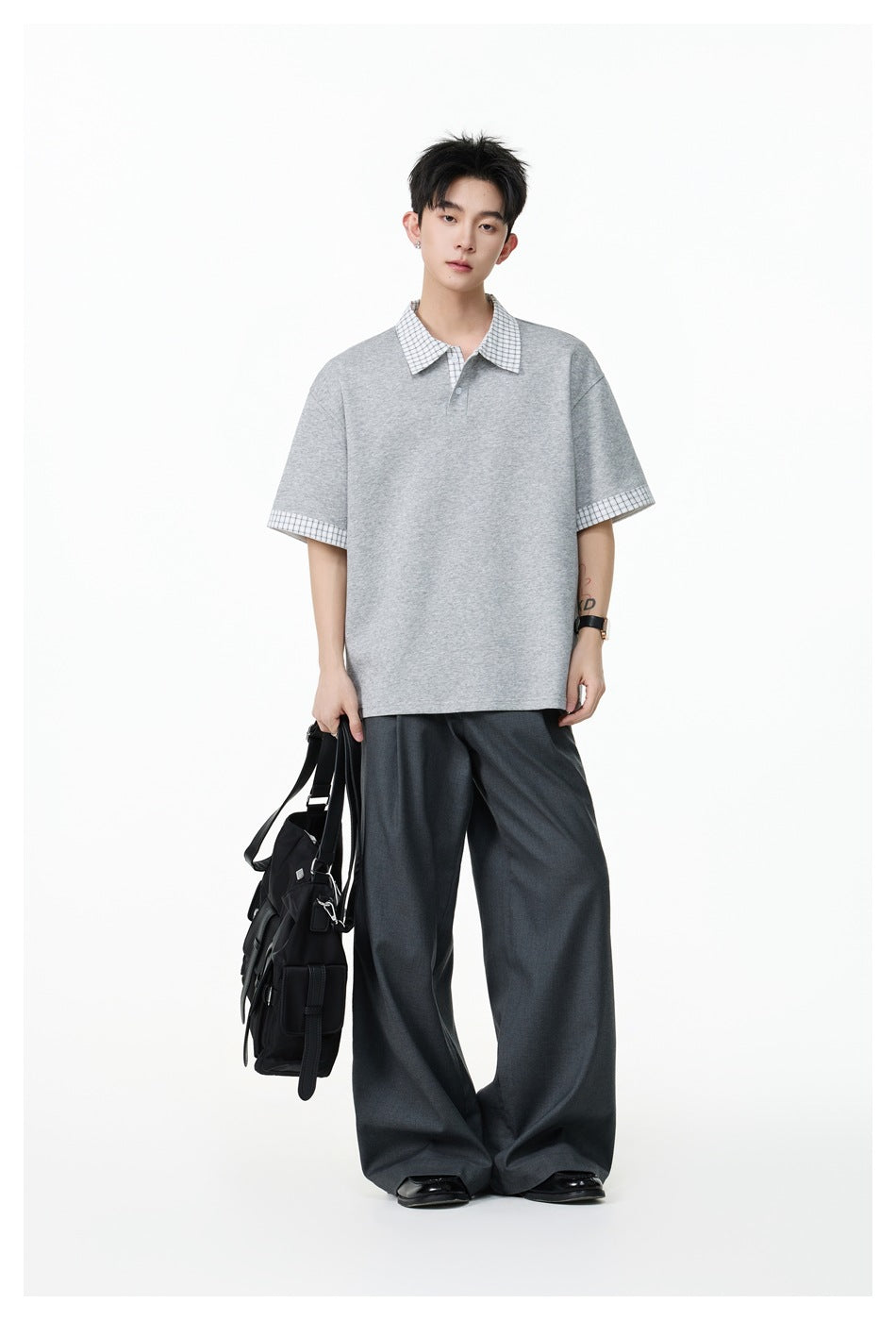 Model wearing a loose light gray polo with a white checked collar and sleeve cuffs, paired with dark wide-leg trousers.