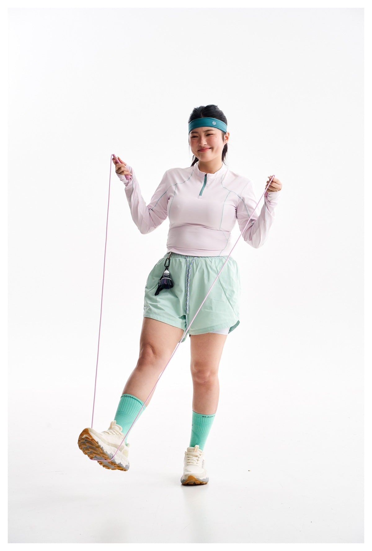 Model wearing a pale pink quarter-zip top and mint shorts while holding a pink exercise rope.