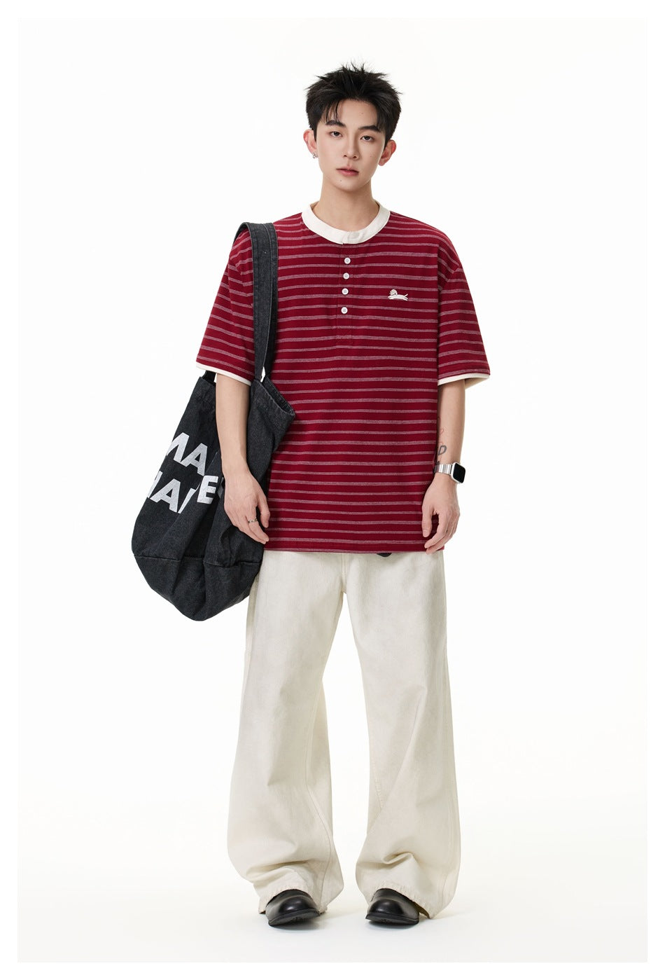 Full-length model wearing a burgundy striped henley with cream trim and loose cream trousers, carrying a dark tote.