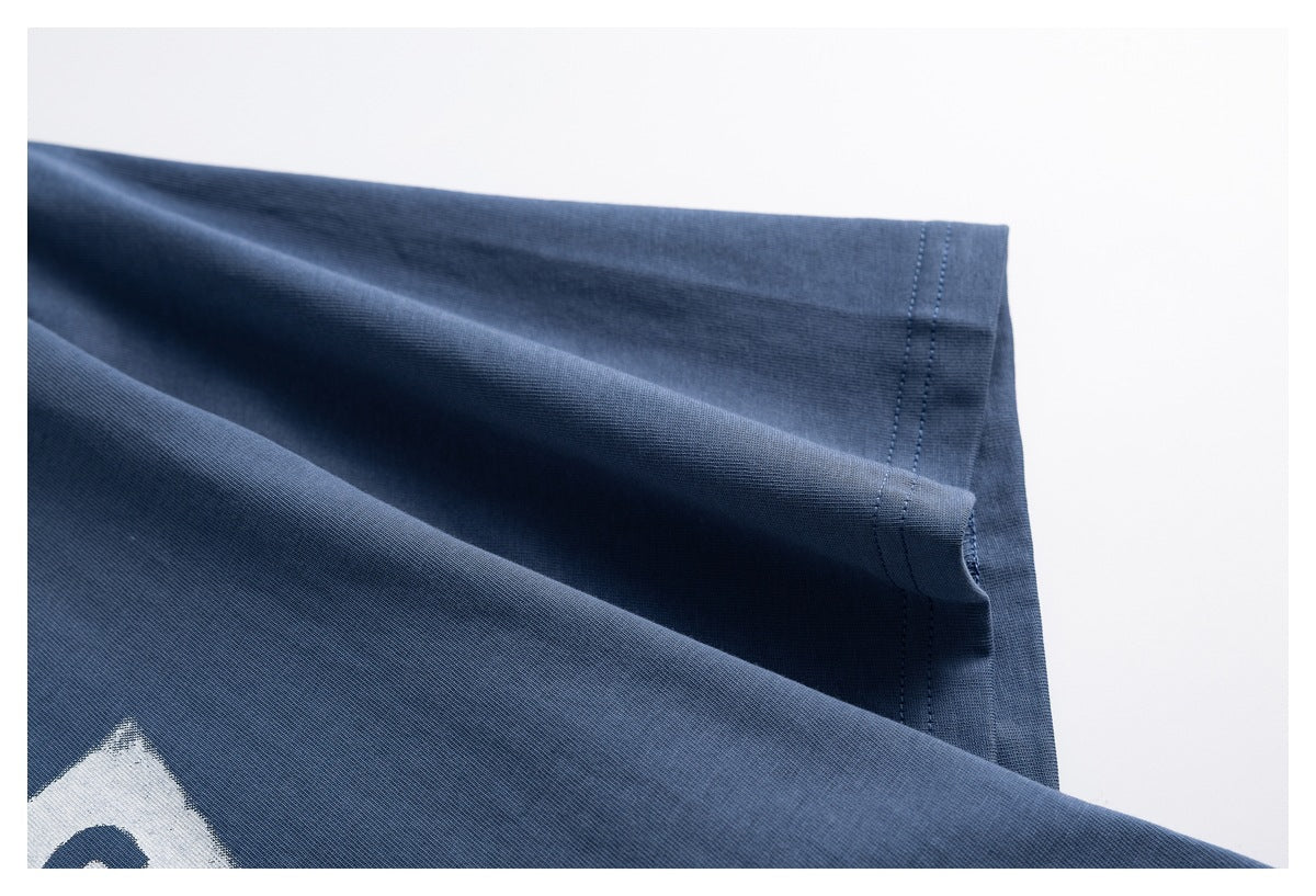 Close-up of the slate-blue T-shirt's short sleeve and double-stitched hem, with part of its white graphic visible.