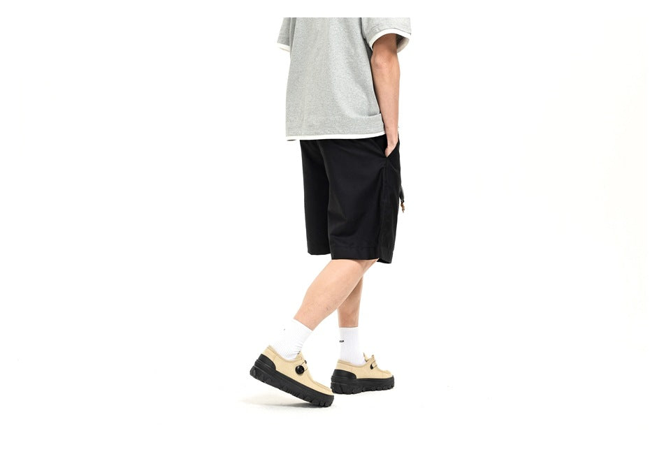 Side view of a model wearing black shorts with a gray T-shirt and beige shoes.