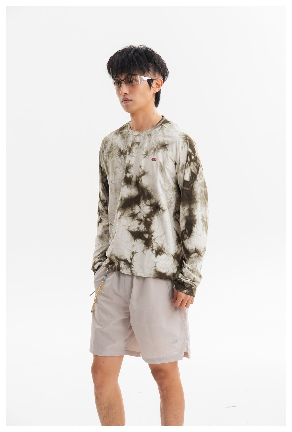 Closer front view of a model wearing an olive-gray tie-dye long-sleeve shirt and pale gray shorts.
