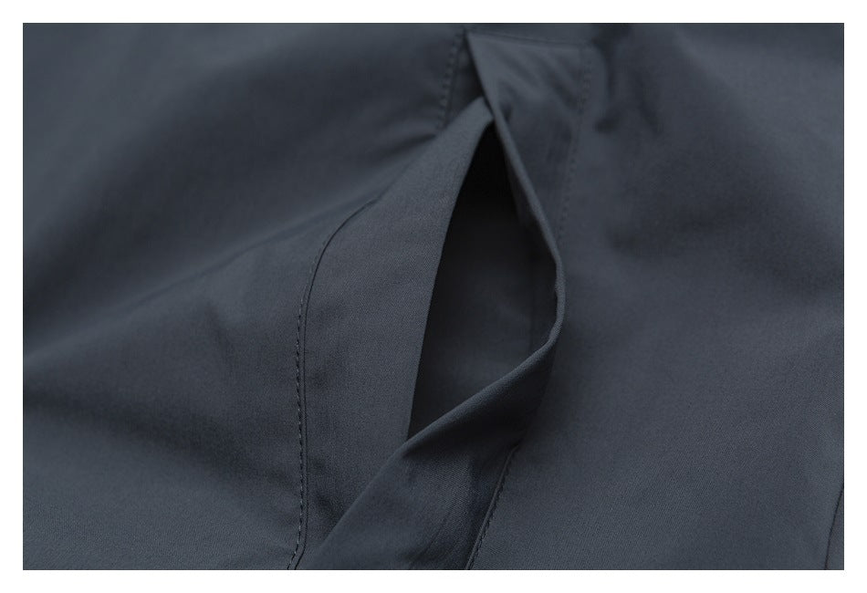 Close-up of a dark charcoal garment’s angled pocket opening and stitched edges.