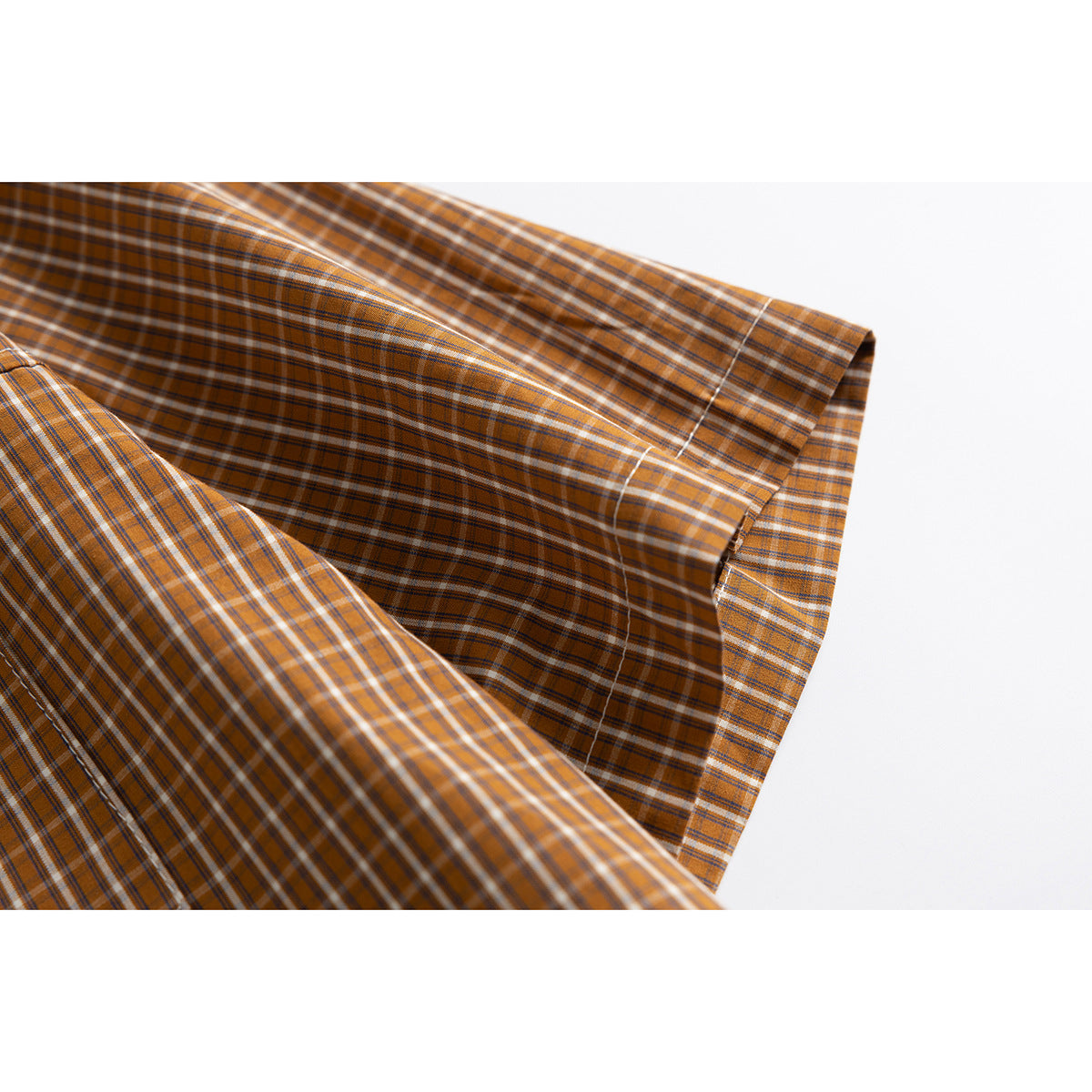 Close-up of the cuff and sleeve of a brown and orange plaid shirt.