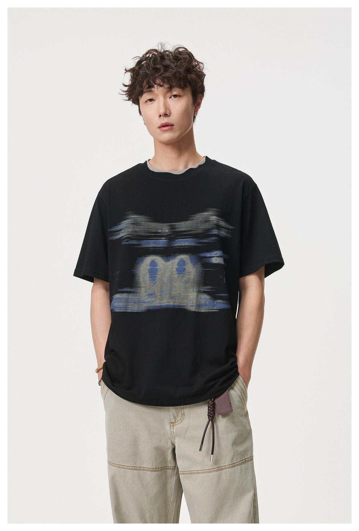 Model wearing a black short-sleeve T-shirt with an abstract blue and gray chest graphic and a layered gray neckline.