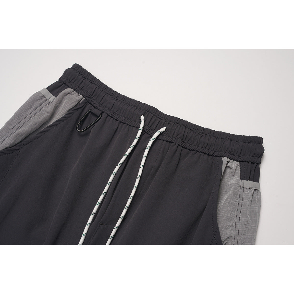 Close-up of charcoal pants showing an elastic waistband, white drawstrings, gray side panel, and small black clip.