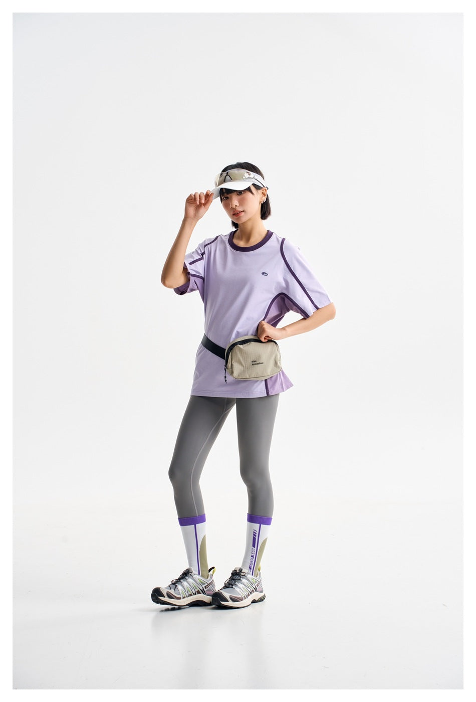 Model wearing an oversized lavender T-shirt with dark trim and charcoal leggings, standing in a studio.