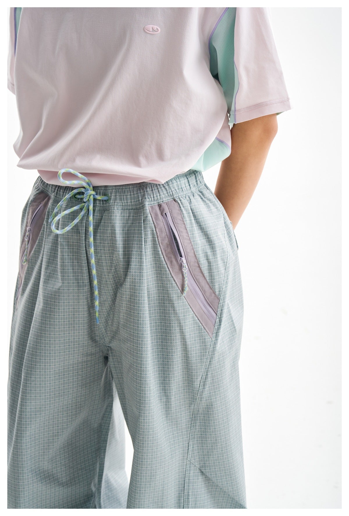 Close-up of pale blue-gray check trousers showing the drawstring waist and lavender-trimmed zip pockets.