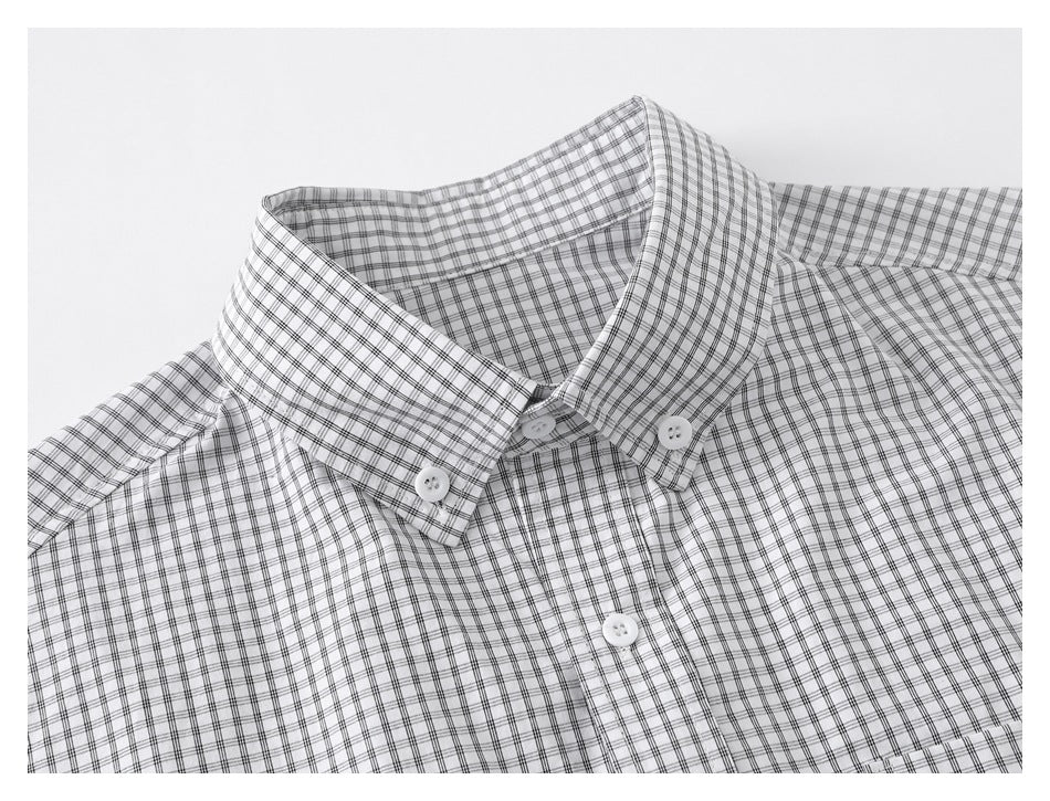 Close-up of the button-down collar and upper front of a white shirt with a fine black grid plaid.