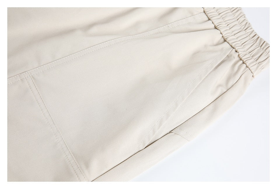 Close-up of light beige pants showing stitched panel seams beside the elastic waistband.