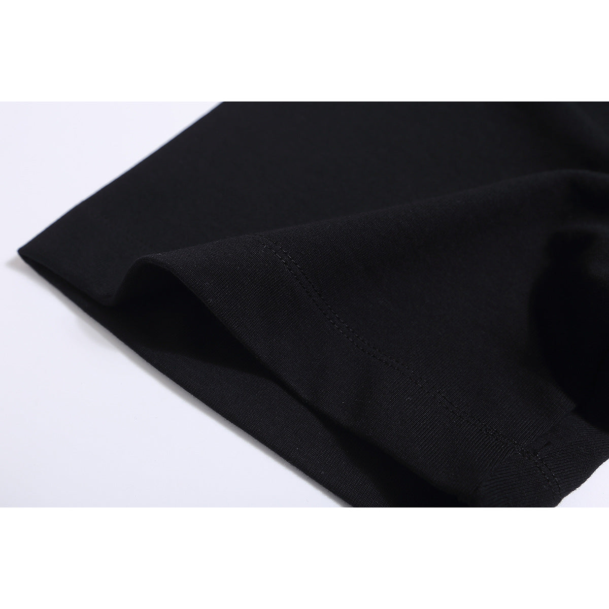 Close-up of black T-shirt fabric and stitched sleeve or hem edging against a white background.