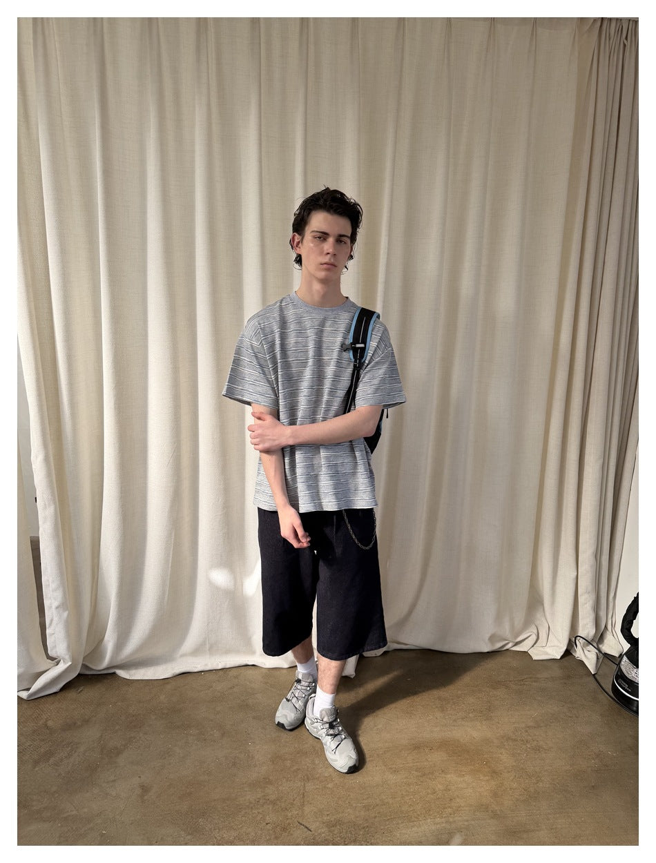 Model wearing a loose gray T-shirt with white and blue stripes, shown with black shorts.
