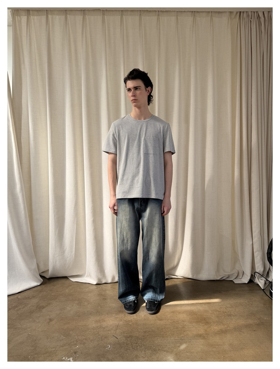 Model facing forward in a gray-and-white striped short-sleeve T-shirt and faded wide-leg blue jeans.