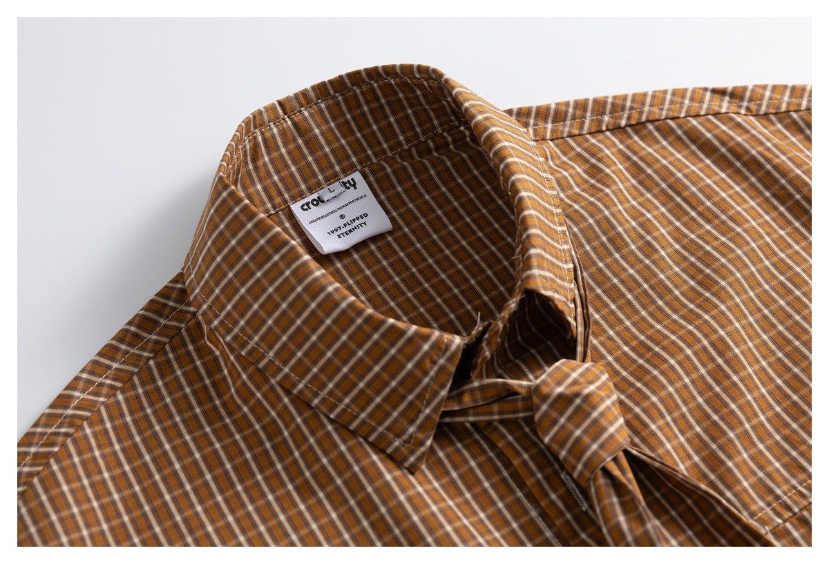 Close-up of a brown, cream, and dark plaid shirt collar with a visible woven neck label and matching tie.