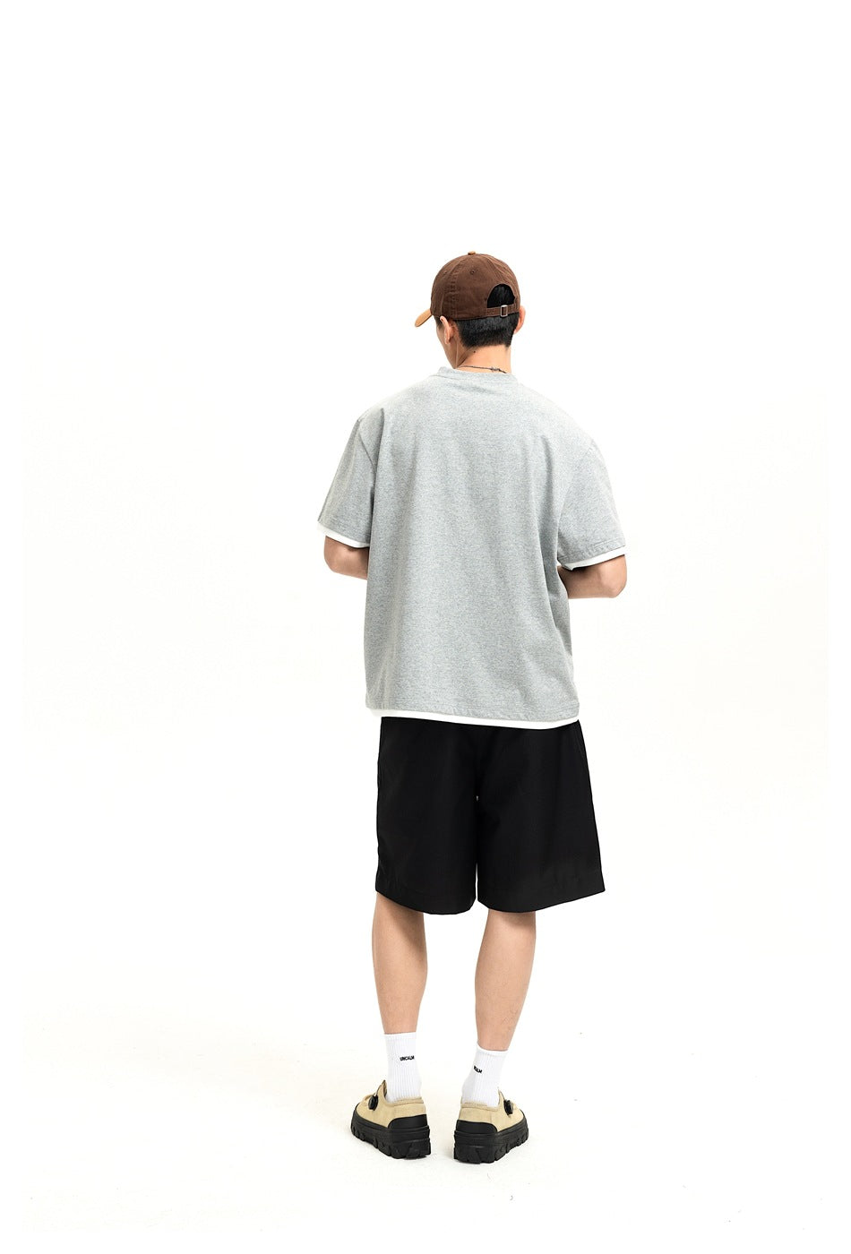 Back view of a model wearing black shorts and a light gray short-sleeve shirt.