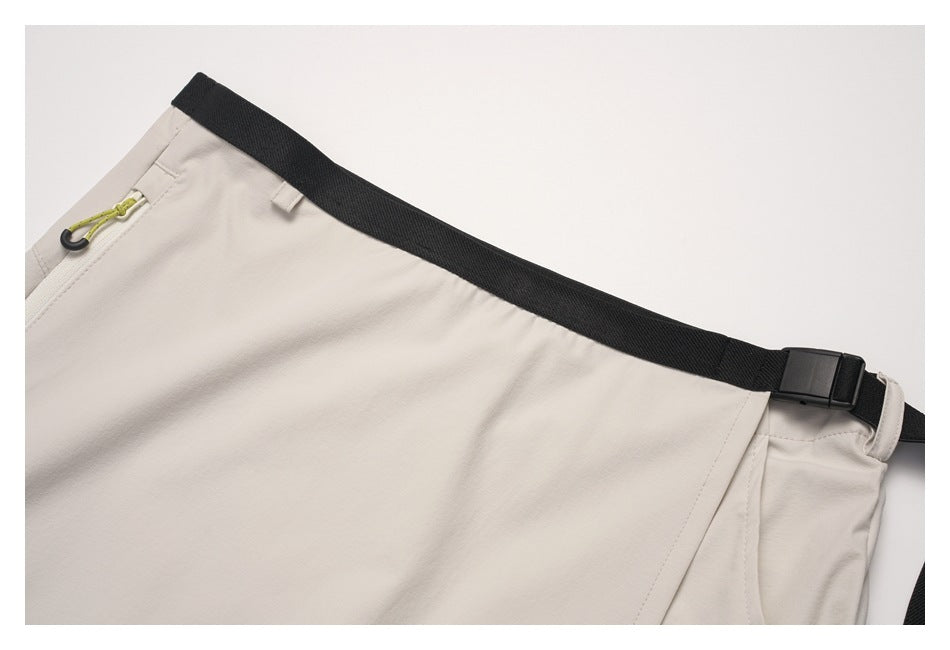Close-up of the beige skirt's black adjustable waist strap, buckle, and zippered pocket with a green pull.