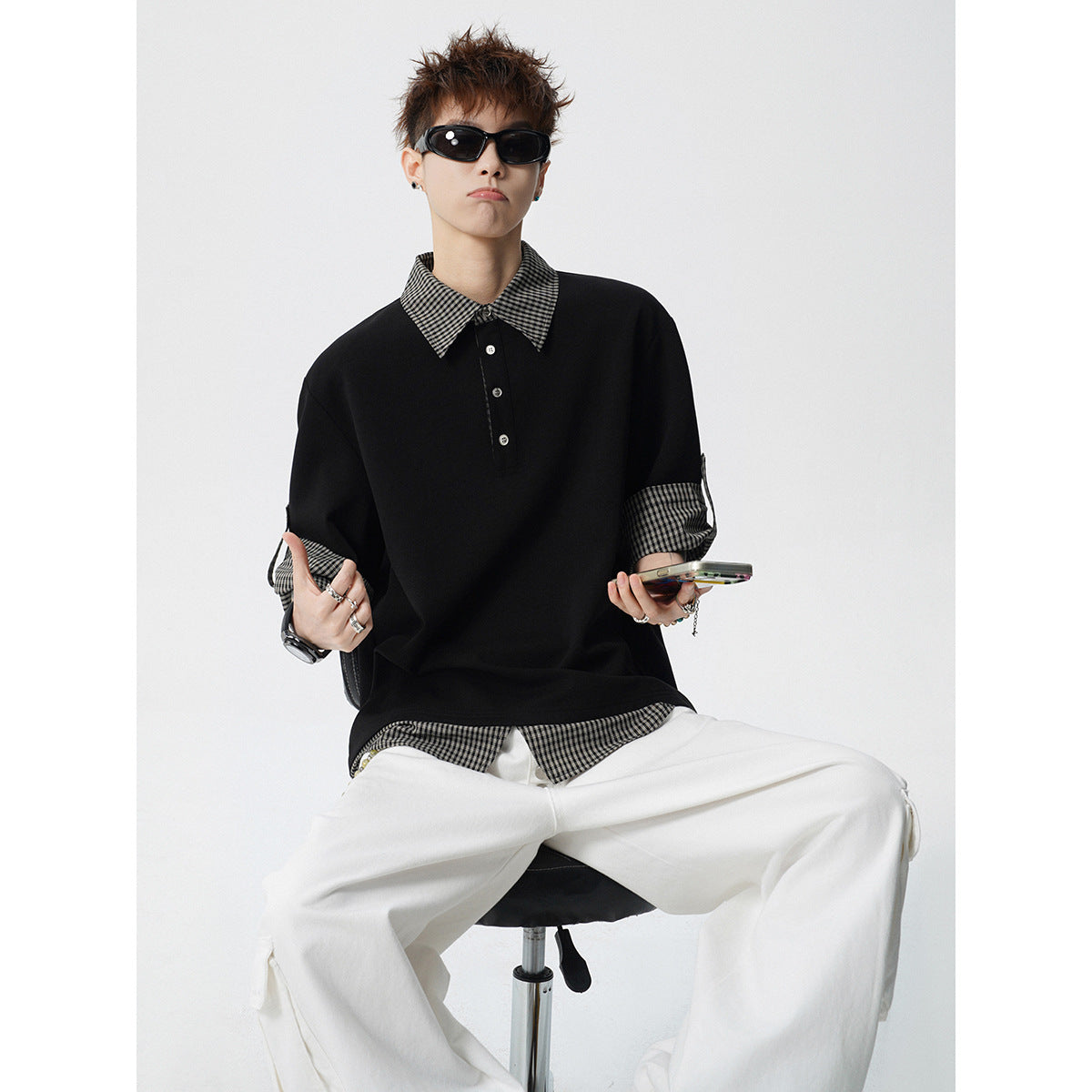 Model seated in a black short-sleeve polo with checked collar, cuffs and hem, paired with white trousers.