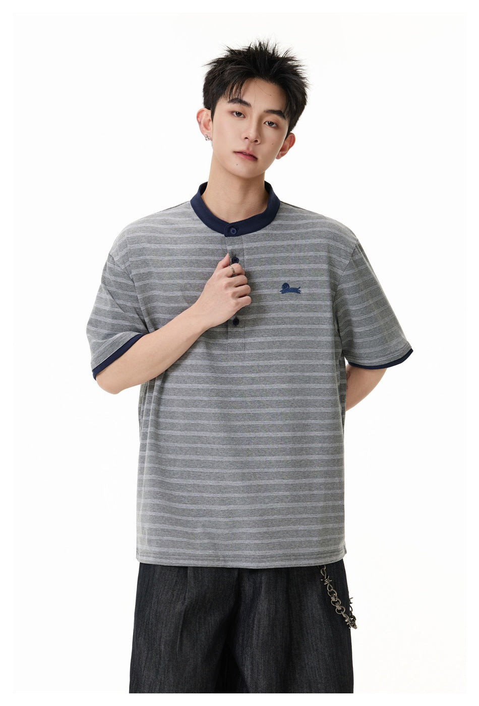 Model in a gray striped henley with navy trim, shown holding the button placket; dark trousers are partly visible.