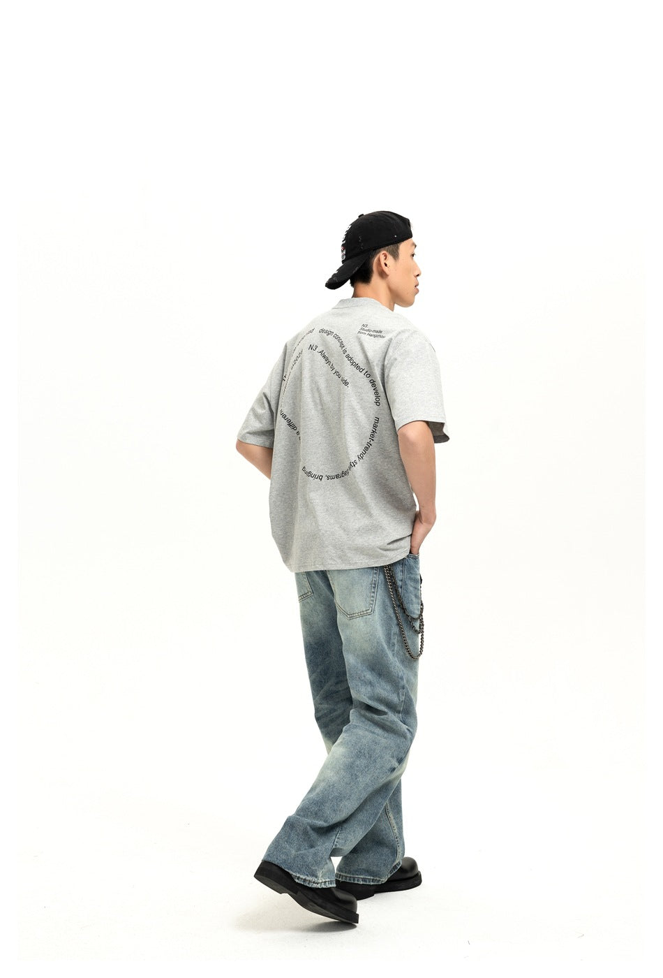 Model seen from the back wearing faded blue wide-leg jeans with a gray printed T-shirt and wallet chain