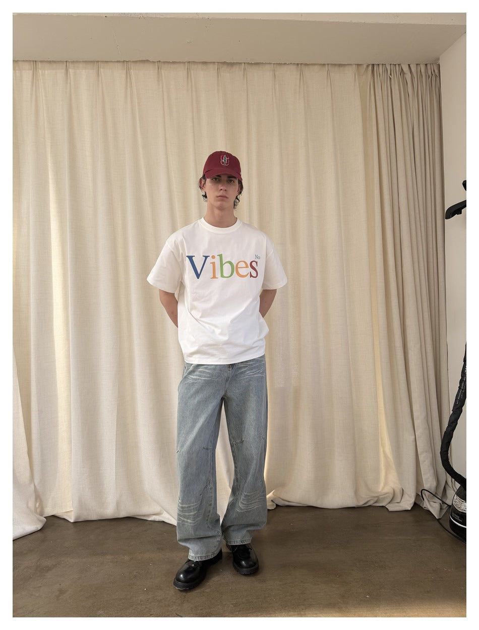 Full-length front view of a model in a white T-shirt with multicolored “Vibes No” lettering and light-wash jeans.