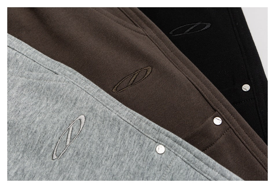 Close-up of three dark brown, black and gray garments with embroidered oval logos and small metal buttons.