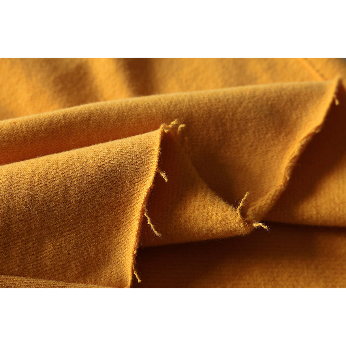 Close-up of folded mustard-yellow fabric showing its inner surface and a raw, frayed edge.