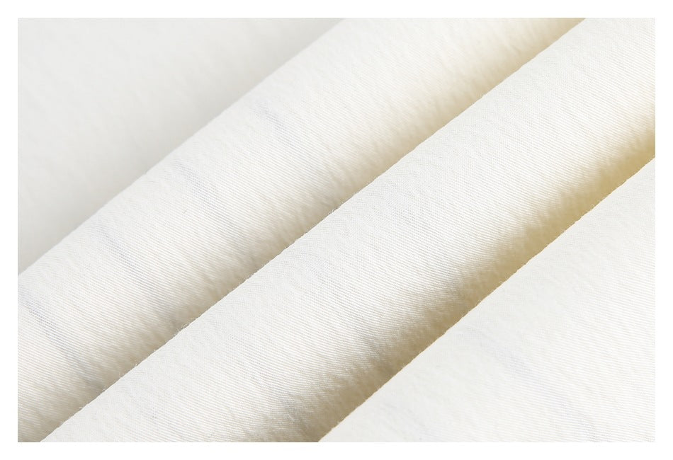 Close-up of ivory garment fabric showing a fine surface texture and softly folded edges.