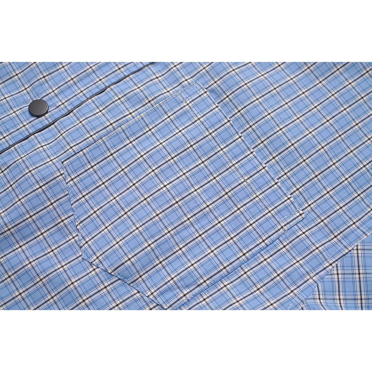 Close-up of a blue plaid shirt's matching chest pocket and a black button.