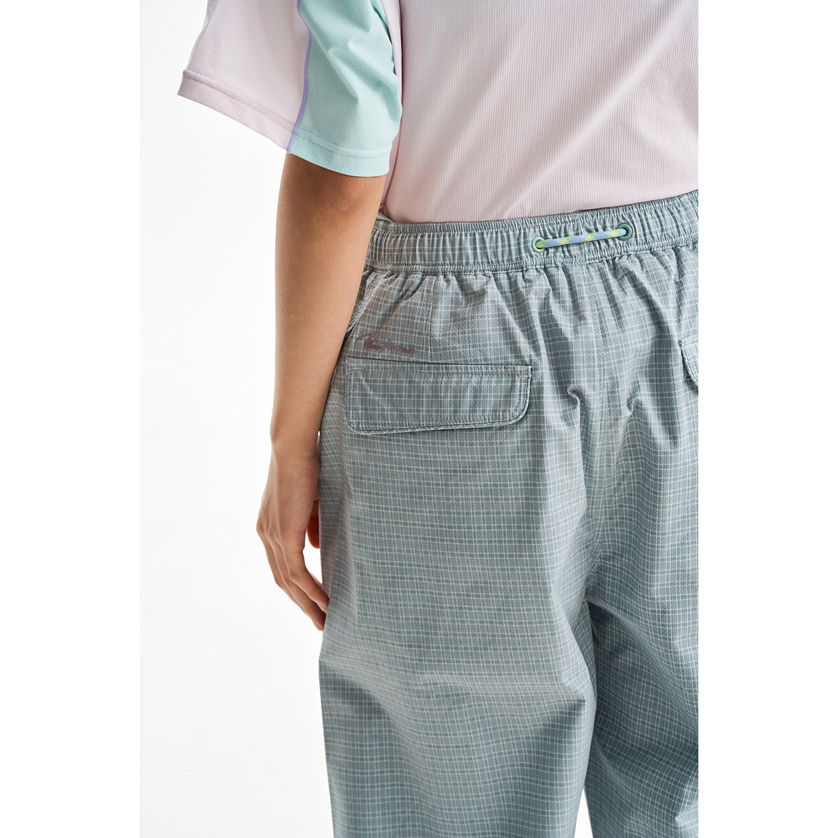 Close-up rear view of pale gray-green plaid pants showing the elastic waist, drawcord, and flap pocket.