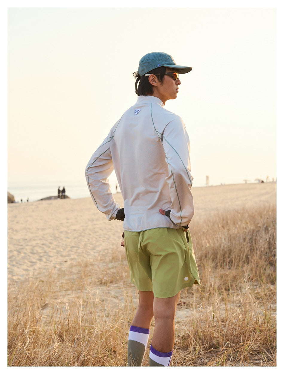 Rear view of a man wearing a pale beige long-sleeve top and olive shorts on a beach.