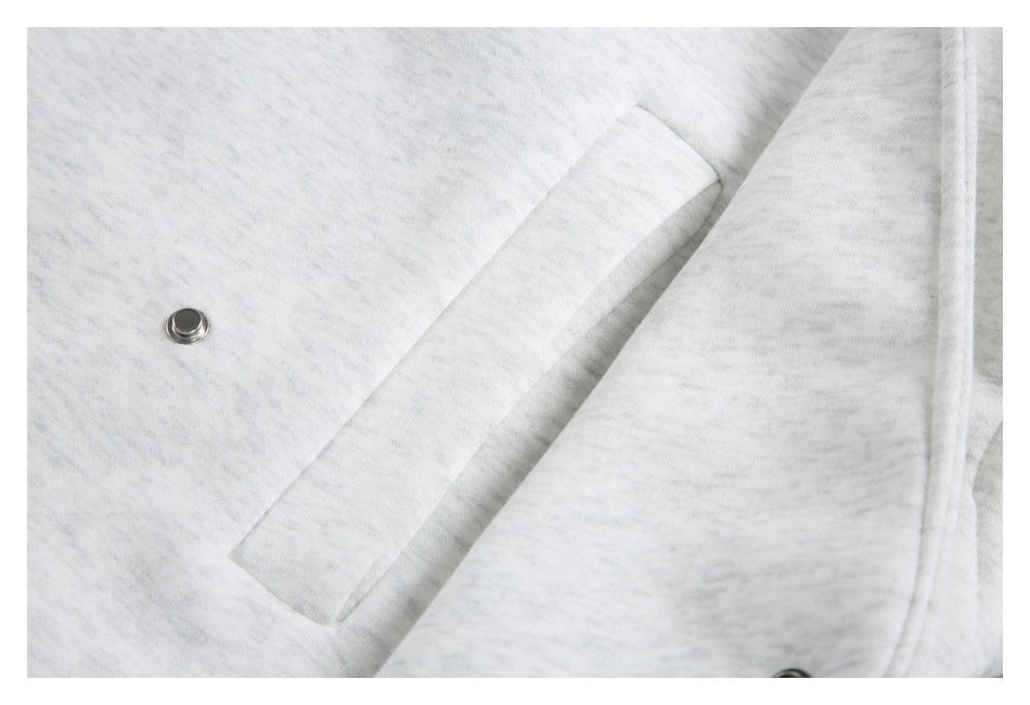 Close-up of a slanted welt pocket and metal snap on the light gray jacket.